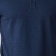Man wearing a navy blue polo shirt and jeans standing against a plain background