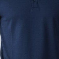 Man wearing a navy blue polo shirt and jeans standing against a plain background