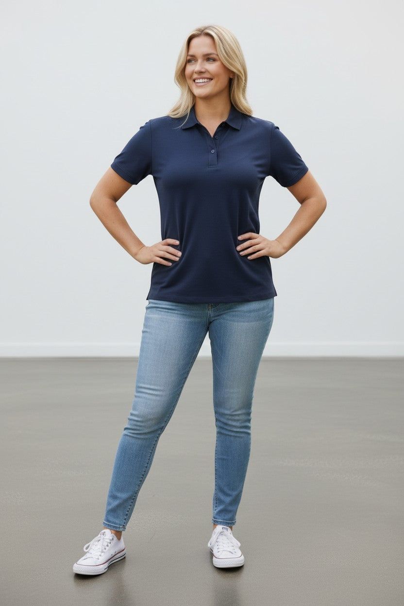 Woman wearing a navy polo shirt and light blue jeans standing against a plain background
