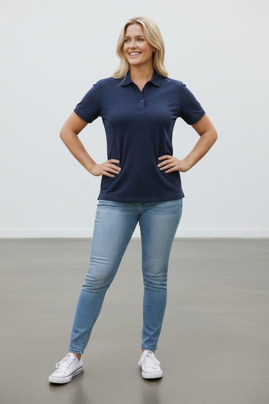 Woman wearing a navy polo shirt and light blue jeans standing against a plain background