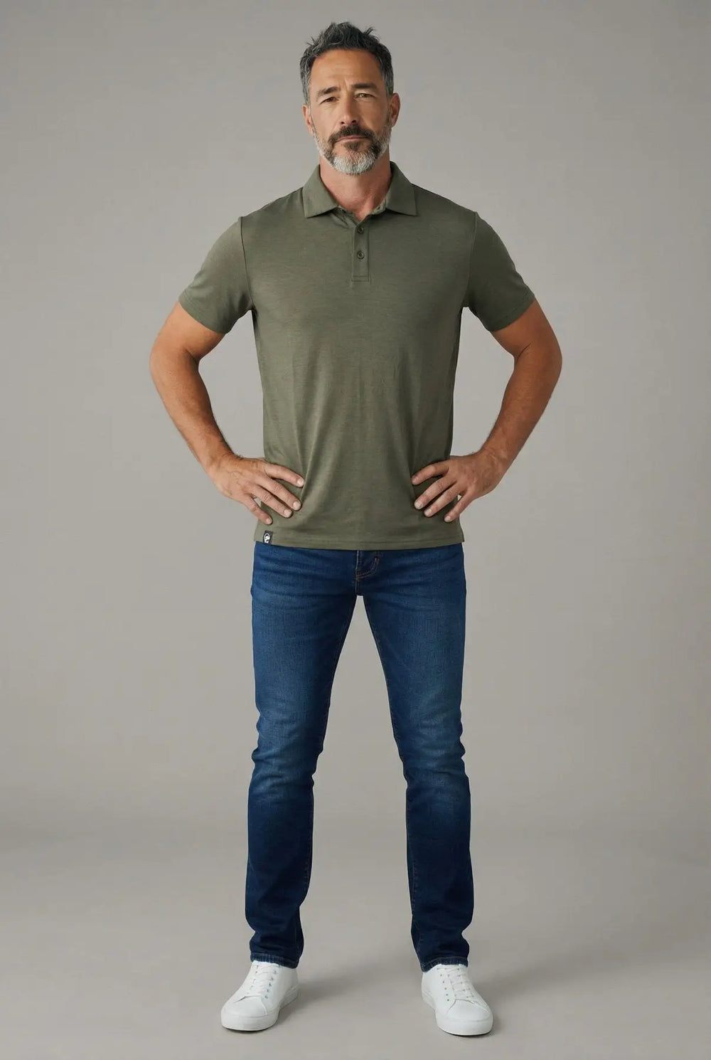 Man wearing a green polo shirt and blue jeans against a gray background