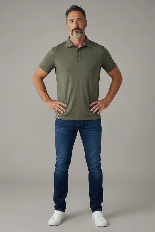 Man wearing a green polo shirt and blue jeans against a gray background