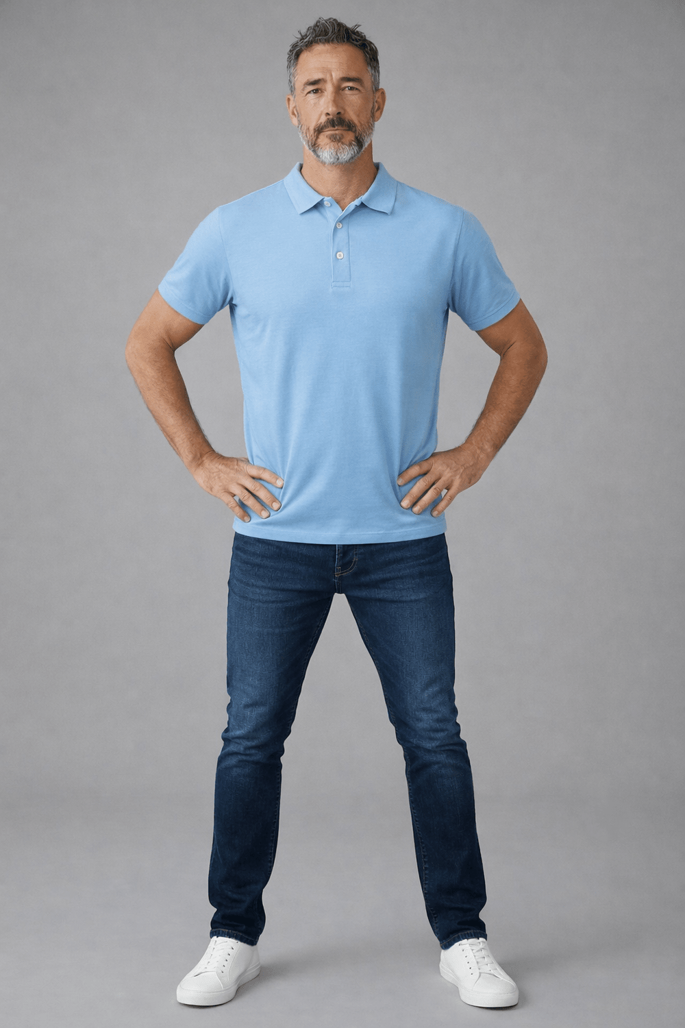 Man wearing a light blue polo shirt and dark blue jeans on a gray background