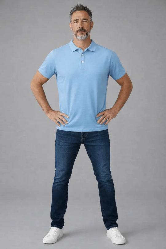 Man wearing a light blue polo shirt and dark blue jeans on a gray background