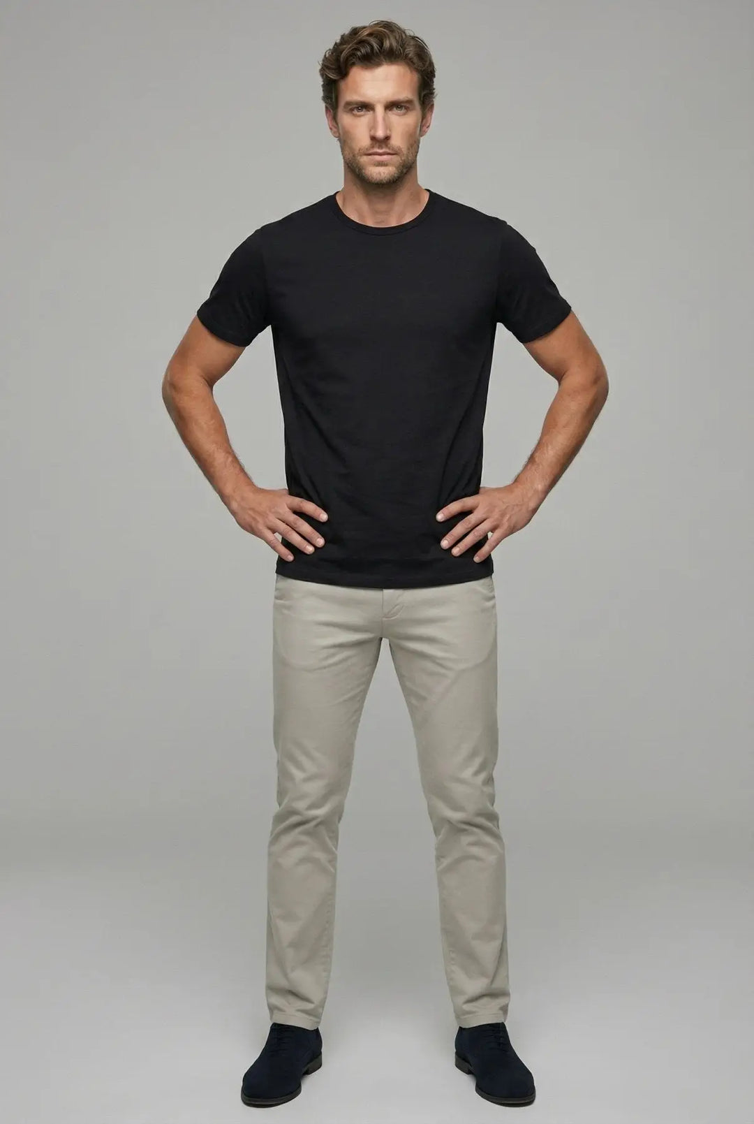 Man wearing a black t-shirt and beige pants against a gray background