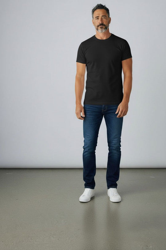 Man wearing a black t-shirt, blue jeans, and white sneakers against a plain background