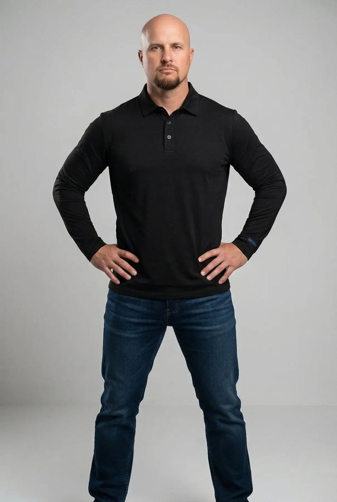 Man wearing a black long-sleeve polo shirt and blue jeans on a gray background
