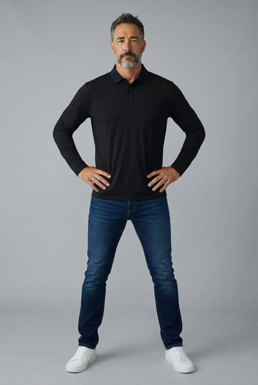 Man wearing a black long-sleeve shirt and blue jeans against a gray background