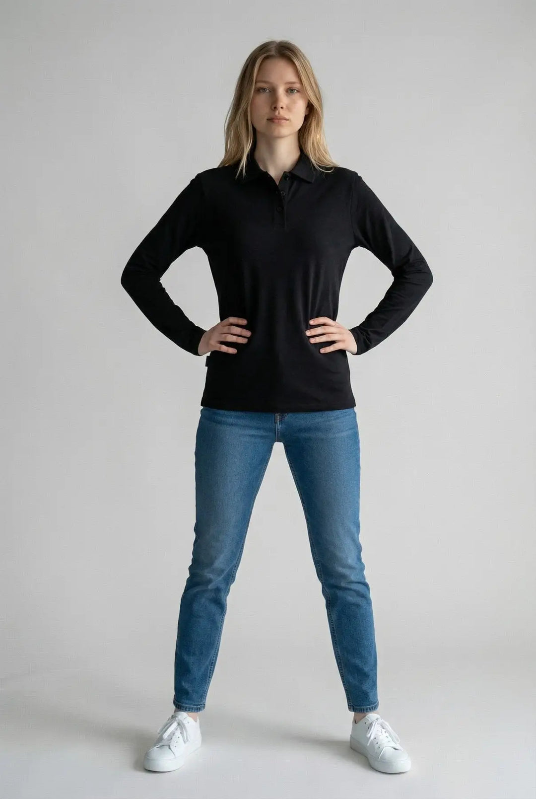 Woman wearing a black long-sleeve shirt and blue jeans on a gray background