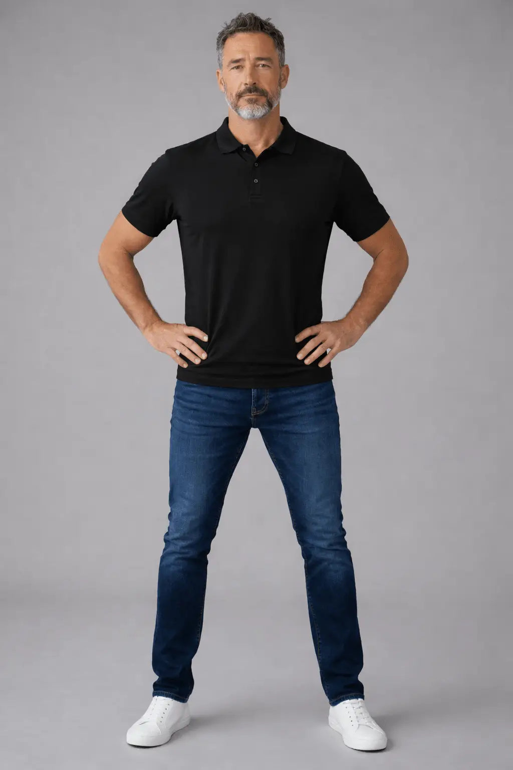 Man wearing a black polo shirt and blue jeans on a gray background