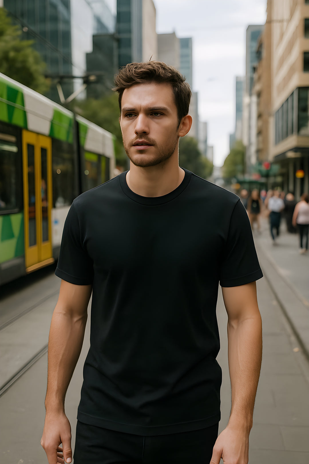 Man wearing a black t-shirt standing on a city street with a tram in the background