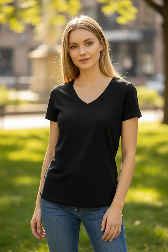 Woman wearing a black merino t-shirt and blue jeans standing outdoors with greenery in the background