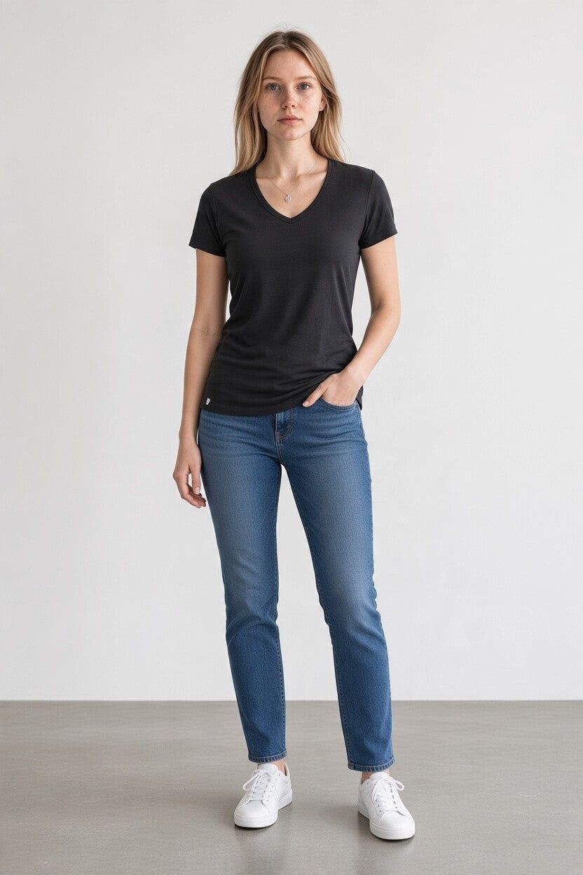A woman modeling a black short-sleeve V-neck t-shirt, blue jeans, and white sneakers against a neutral studio background.