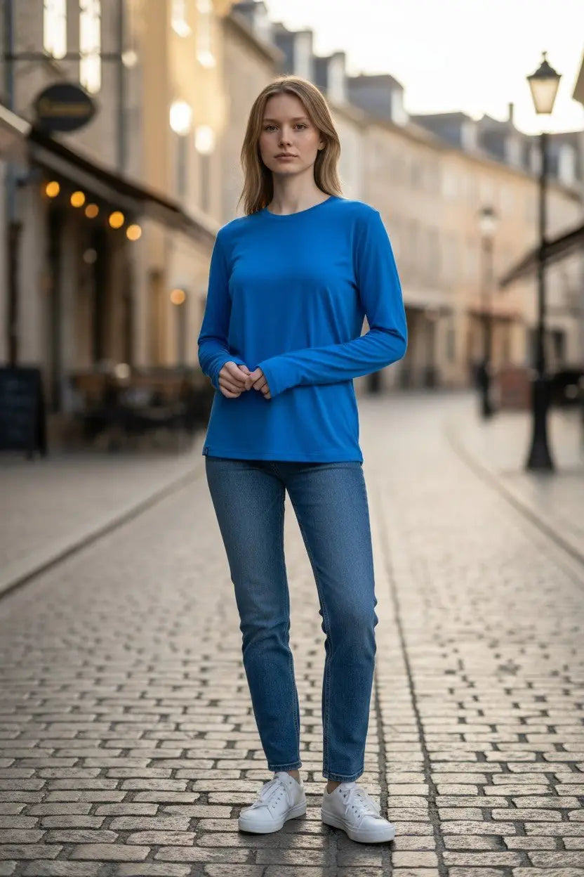 Person wearing a blue long-sleeve shirt and jeans standing on a cobblestone street.
