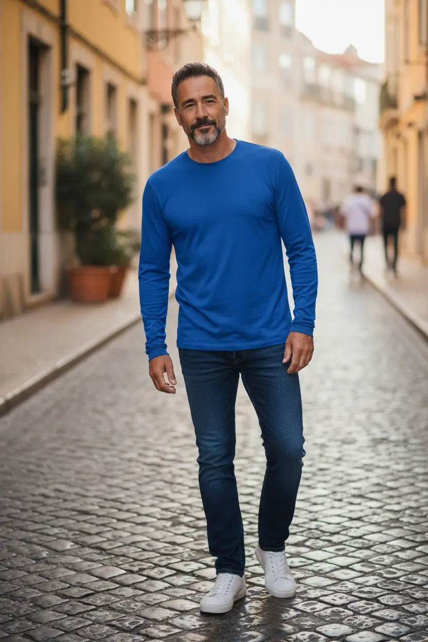 Man wearing a blue long-sleeve shirt and jeans standing on a cobblestone street.