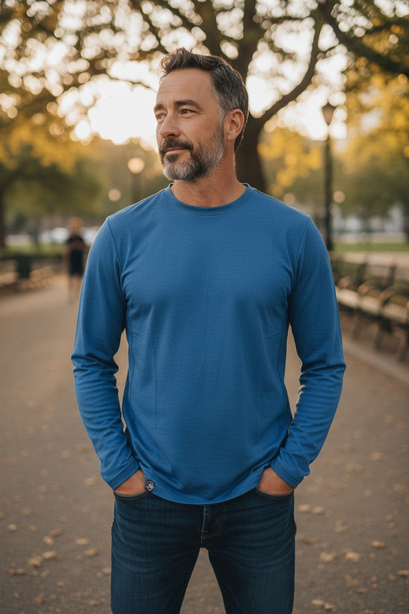 Man wearing a blue long-sleeve shirt standing outdoors with trees and benches in the background