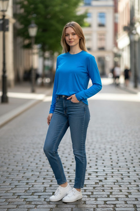 Woman wearing a blue long-sleeve top and jeans standing on a street.