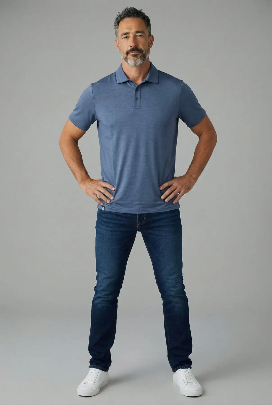 Man wearing a blue polo shirt and jeans on a gray background