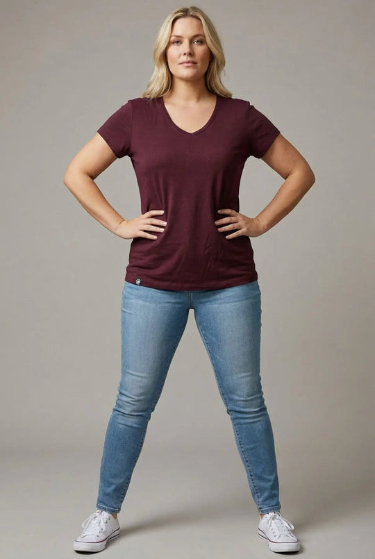 Woman wearing a maroon t-shirt and blue jeans against a plain background