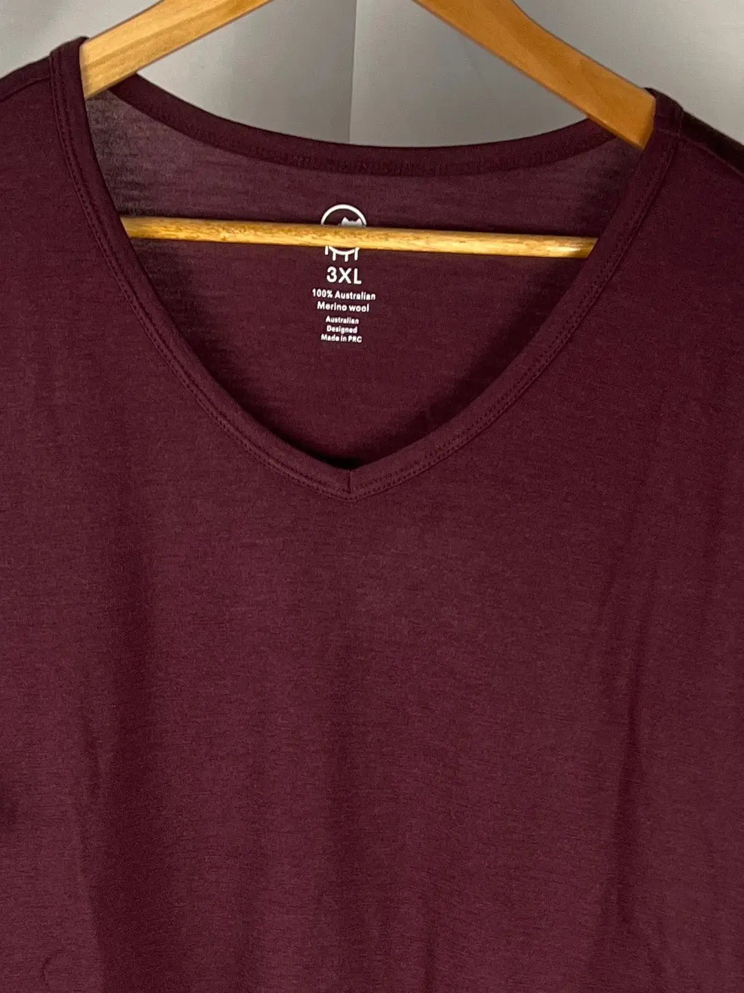 Maroon V-neck t-shirt on a wooden hanger against a neutral background