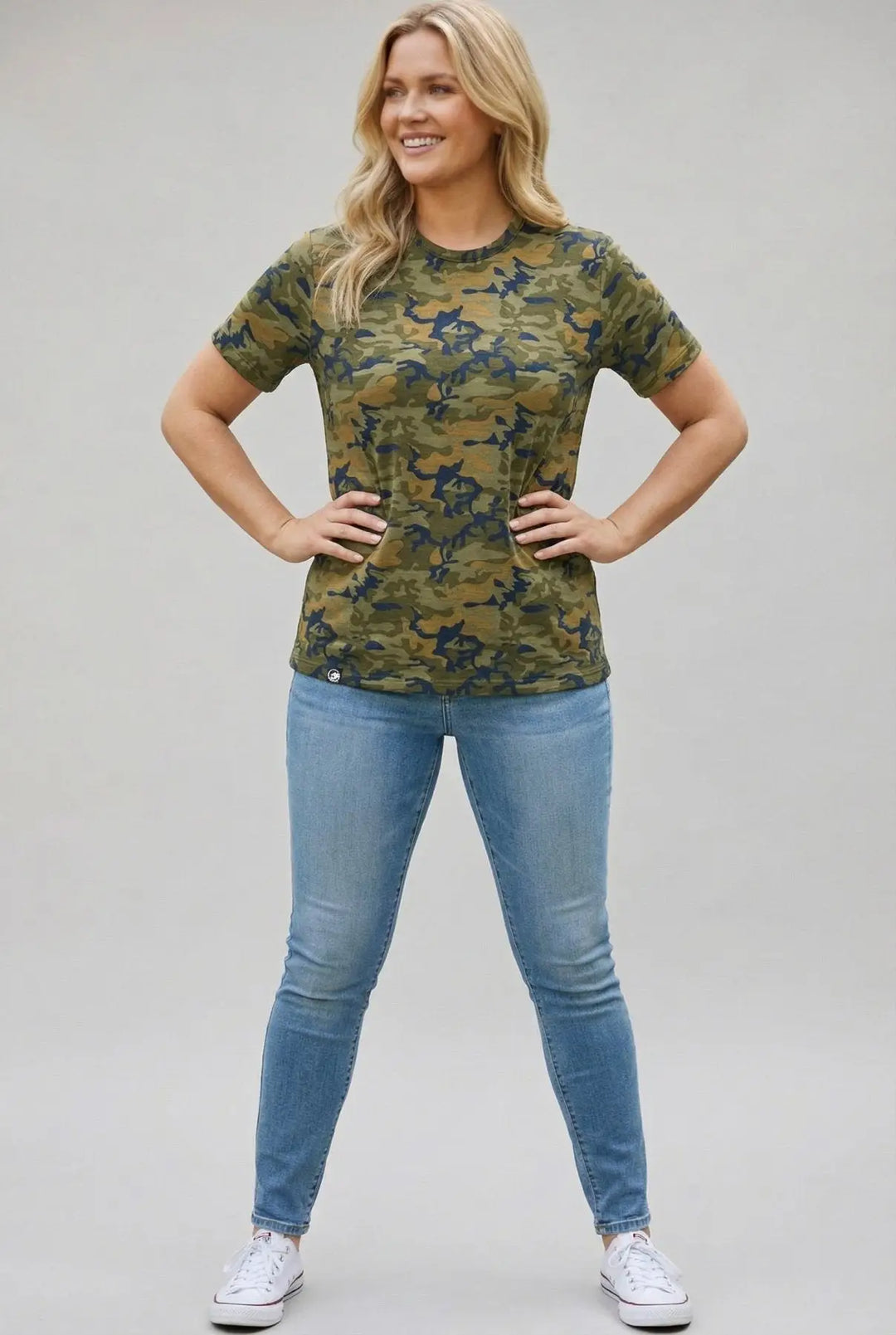 Woman wearing a camouflage t-shirt and blue jeans on a plain background
