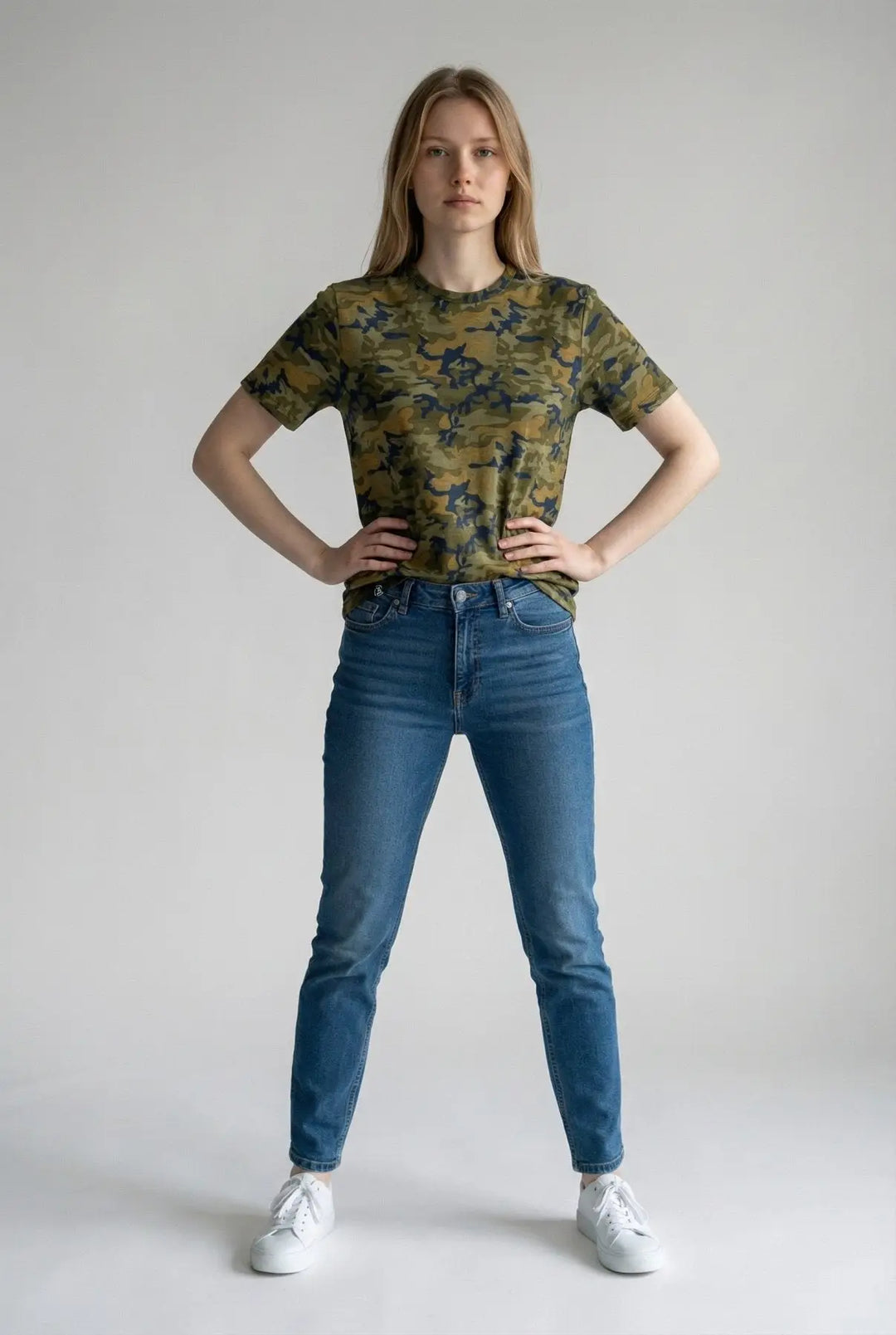Woman wearing a camouflage t-shirt and blue jeans on a plain background