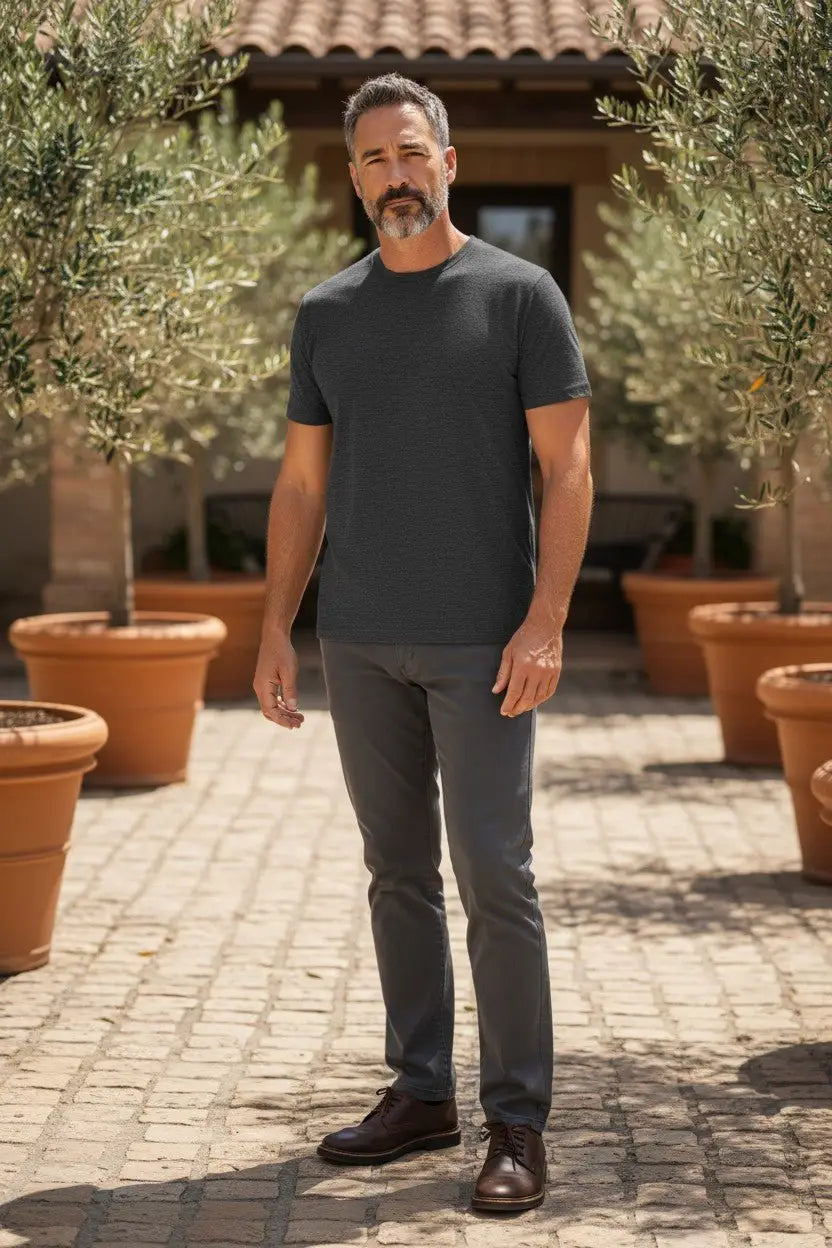 Man in a black t-shirt and gray pants standing outdoors with potted plants and a building in the background.