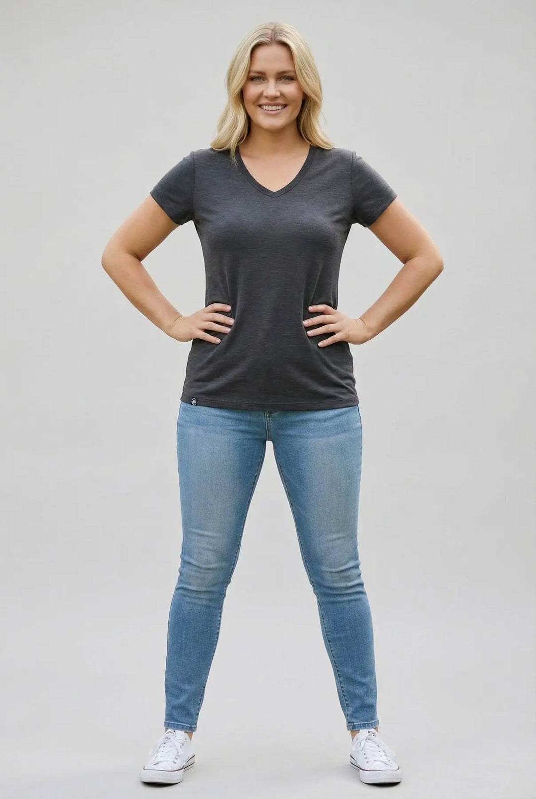 Woman wearing a dark gray t-shirt and blue jeans on a plain background