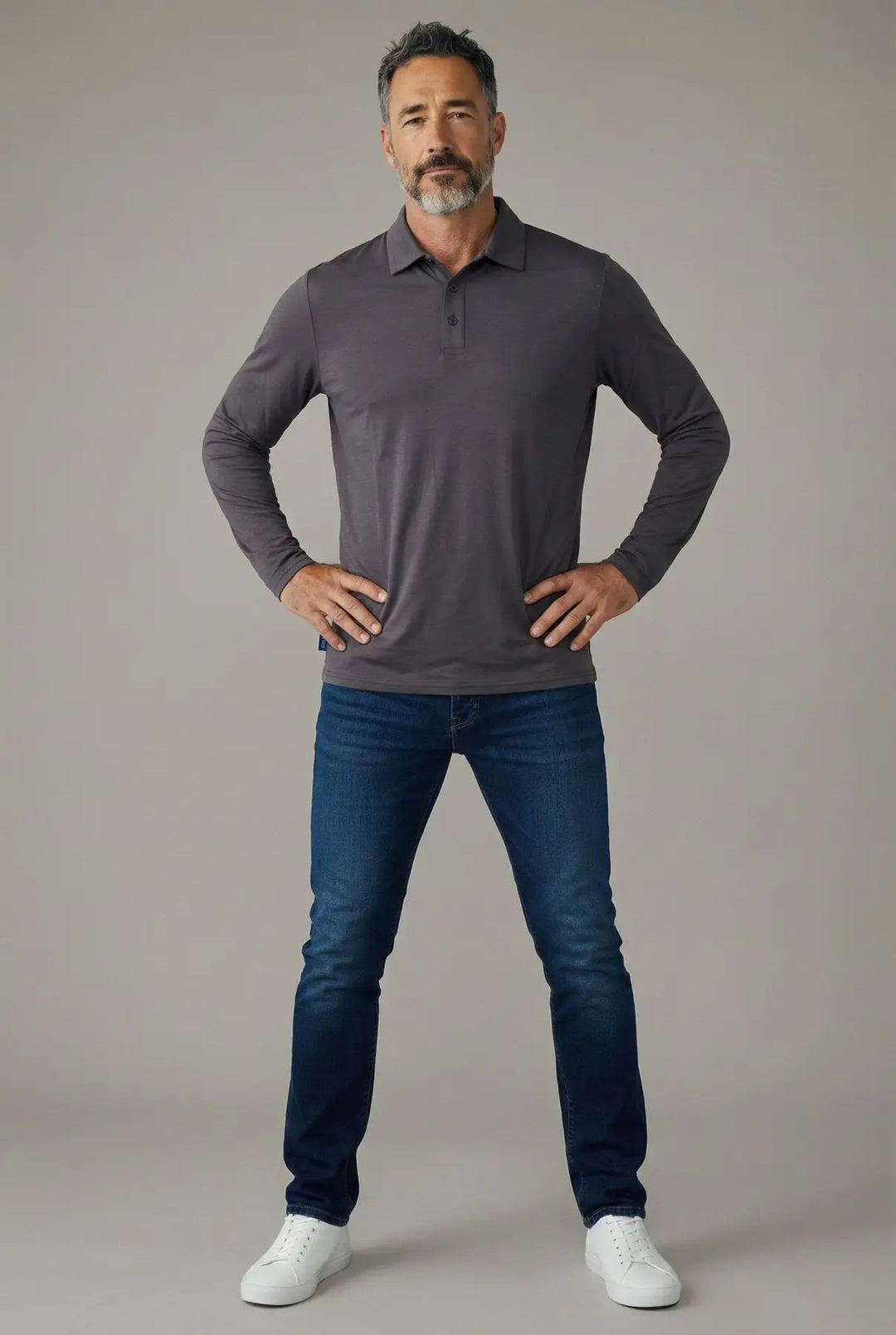Man wearing a gray long-sleeve shirt and blue jeans against a plain background
