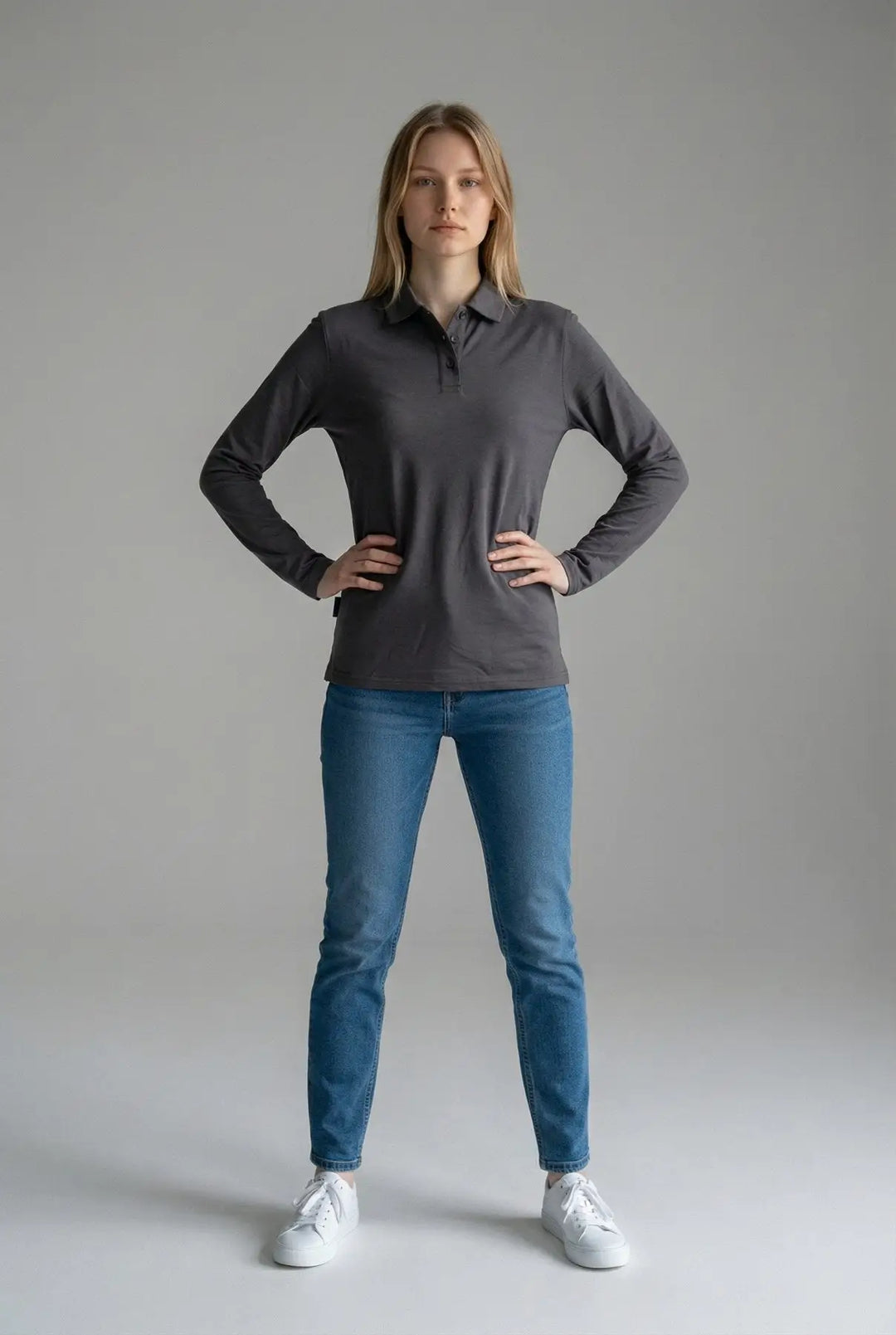 Woman wearing a gray long-sleeve shirt and blue jeans on a gray background