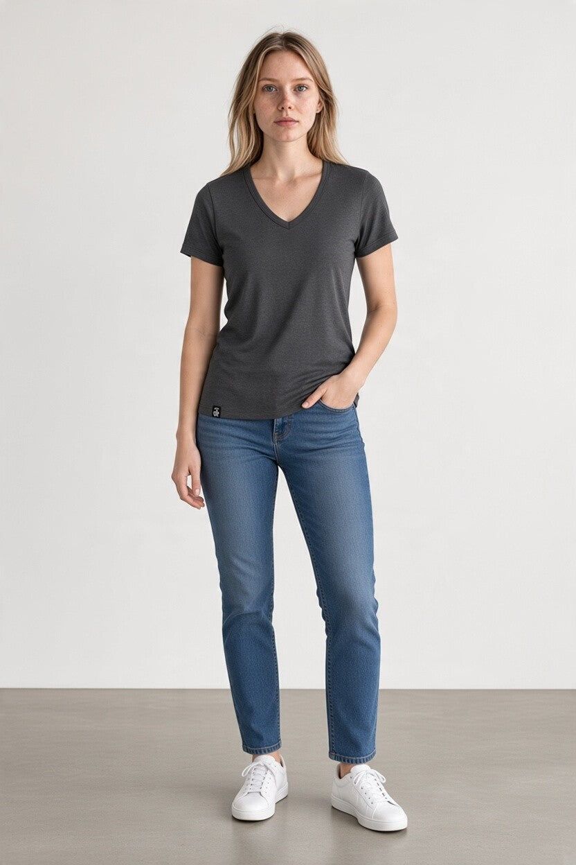 A woman modeling a dark gray v-neck t-shirt, blue jeans, and white sneakers against a neutral studio background.