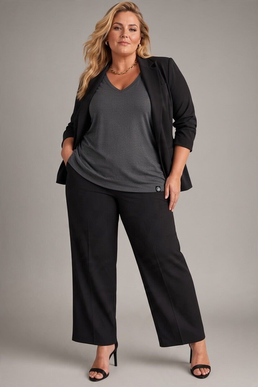 A woman modeling a black wide-leg blazer and matching wide-leg trousers over a charcoal gray V-neck top, paired with black heeled sandals, against a solid gray studio background.