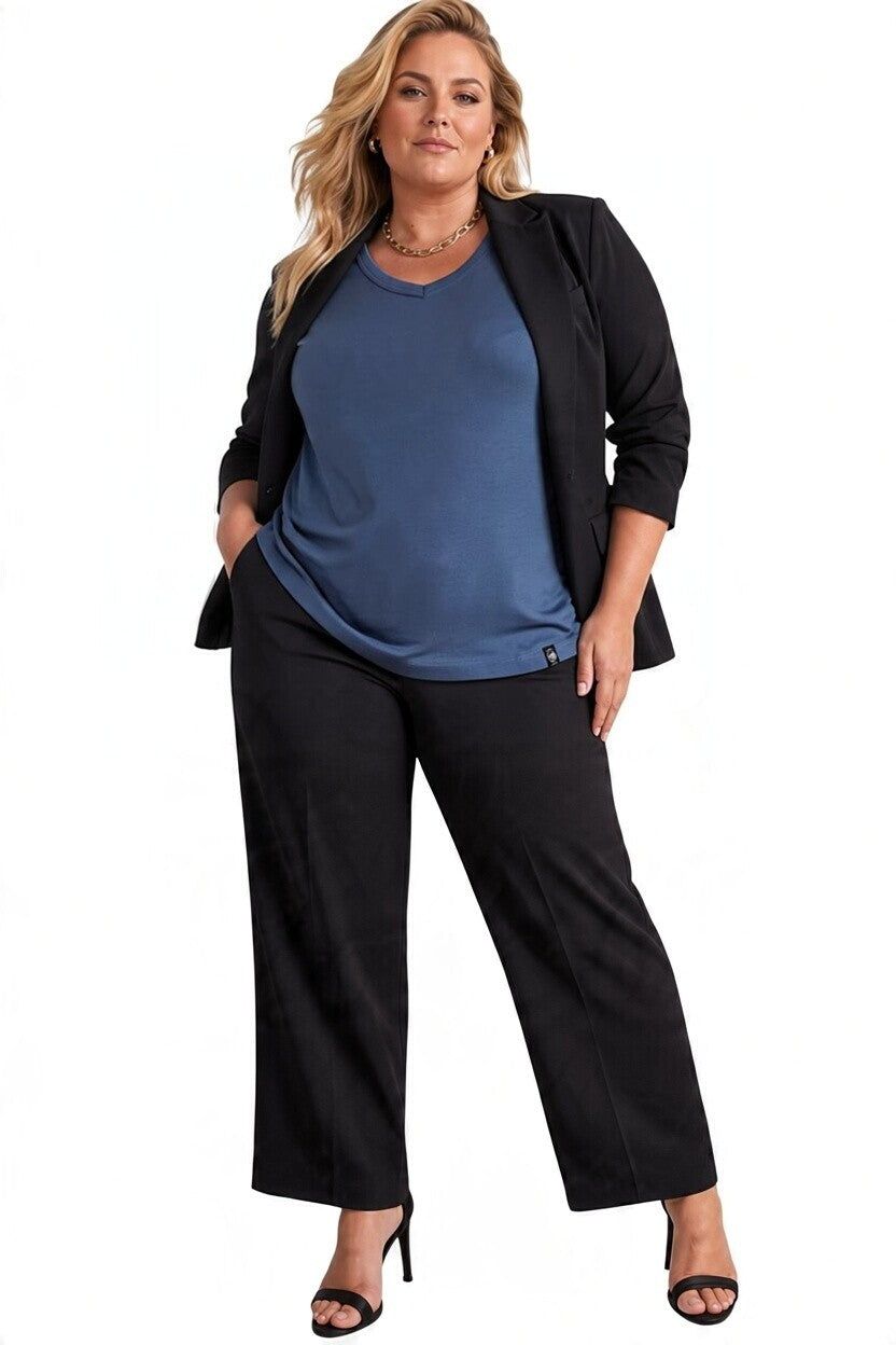 A plus-size woman modeling a black wide-leg pants set with a black blazer and a slate blue top, standing against a plain white background.