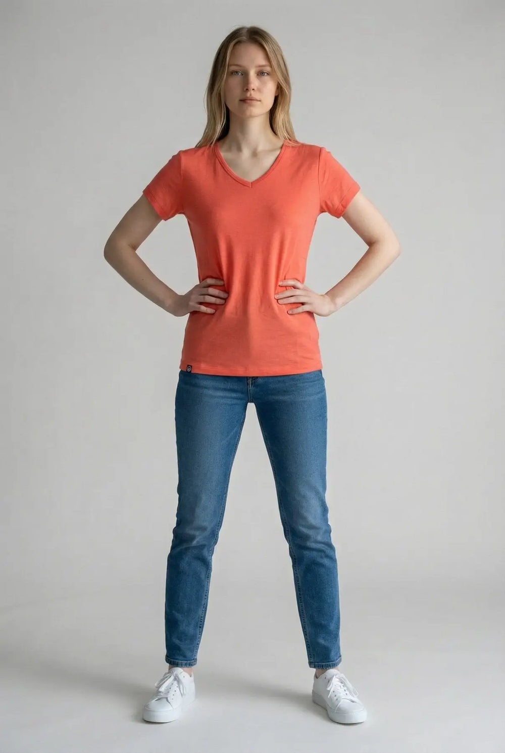 Woman wearing an orange t-shirt and blue jeans on a plain background