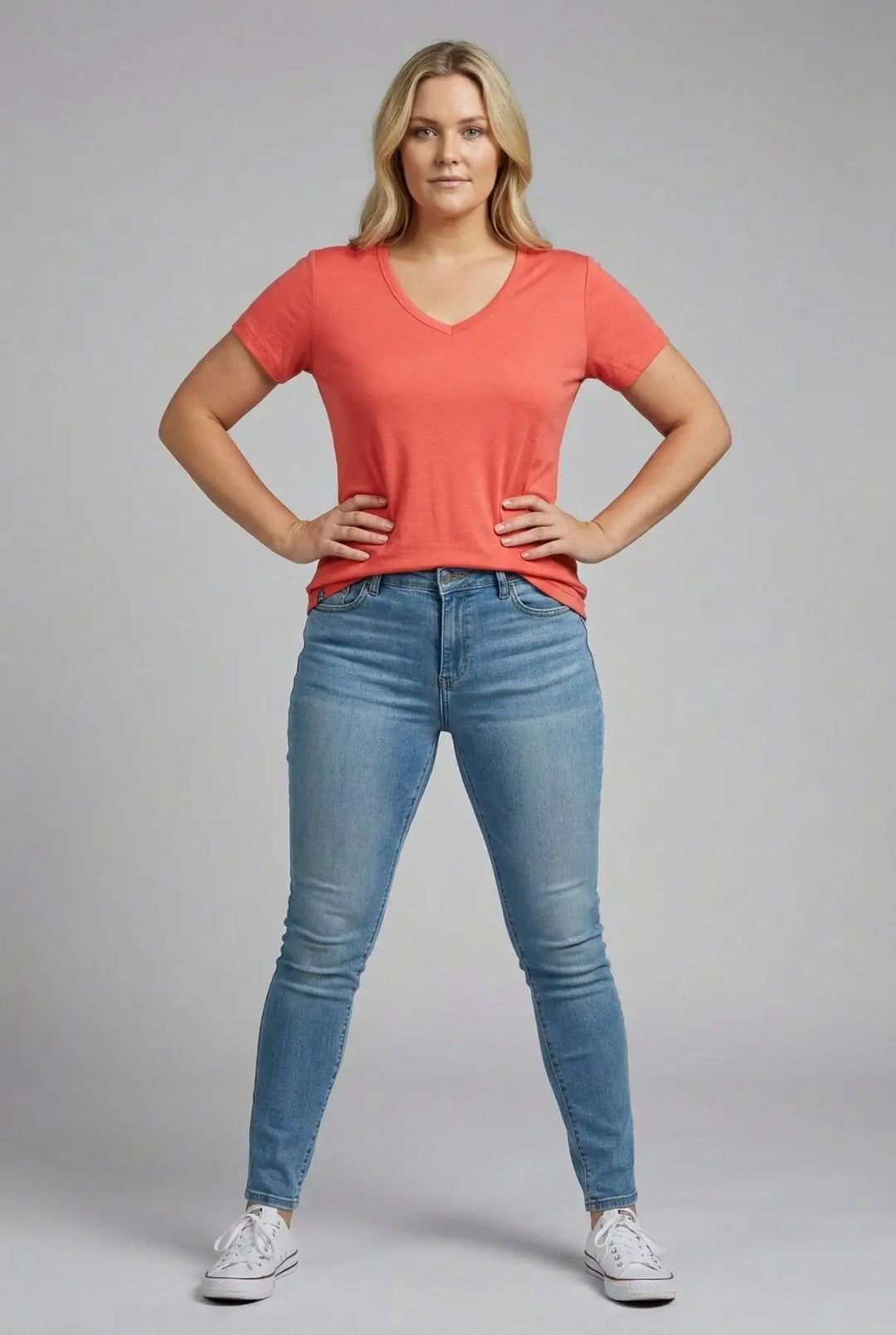 Woman wearing a coral t-shirt and blue jeans on a gray background
