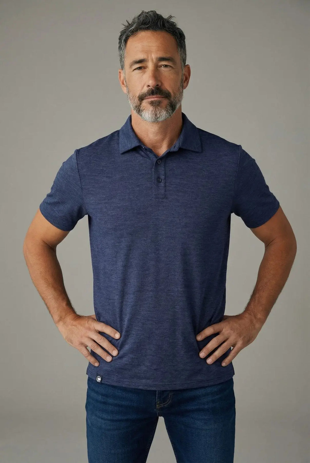 Man wearing a blue polo shirt and jeans against a gray background