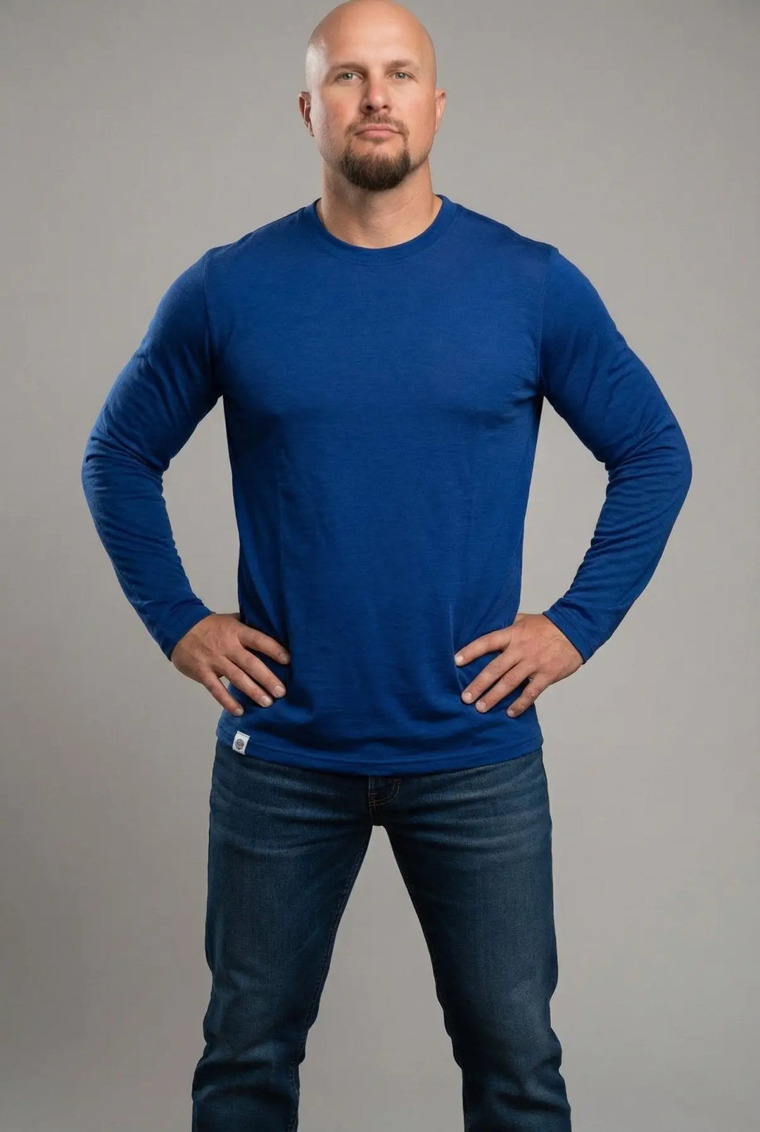 Man wearing a blue long-sleeve shirt and jeans against a gray background