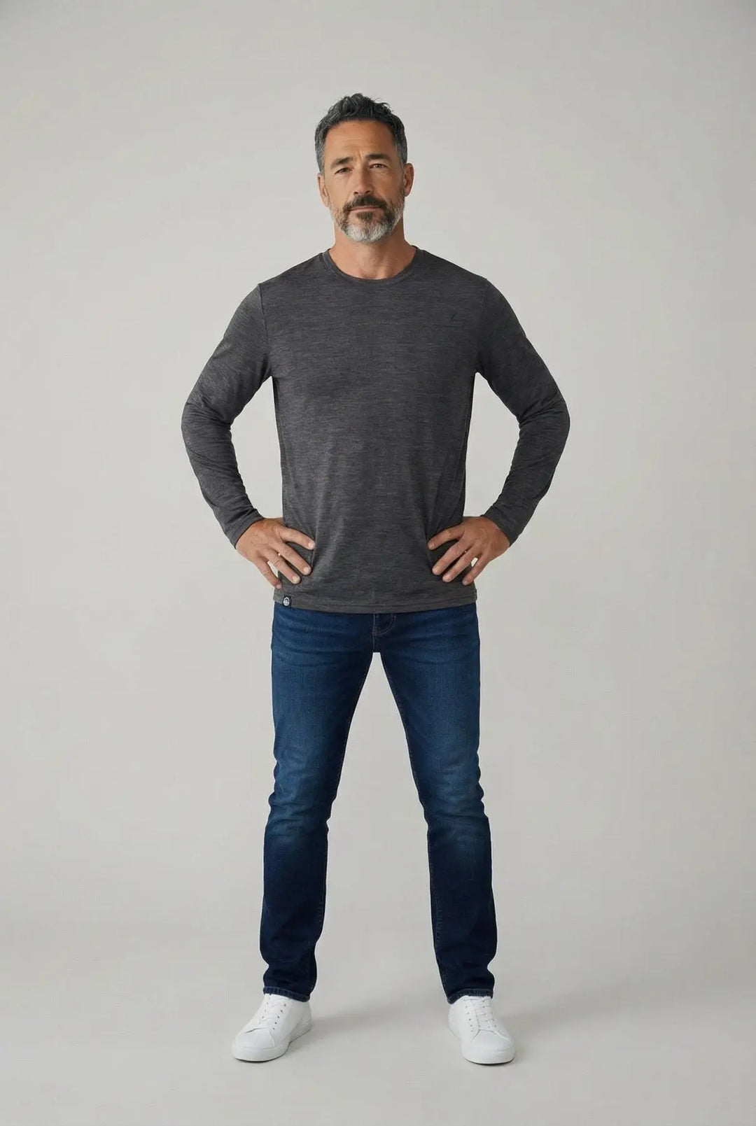 Man wearing a dark gray long-sleeve shirt and blue jeans on a light gray background