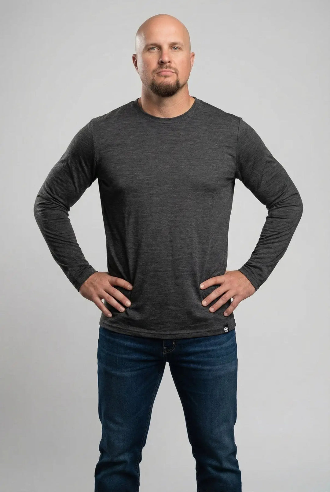 Man wearing a dark gray long-sleeve shirt and blue jeans against a light gray background