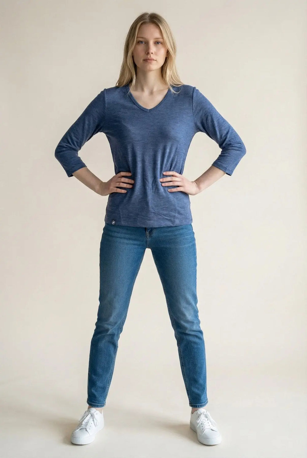 Woman wearing a blue shirt and jeans standing against a plain background