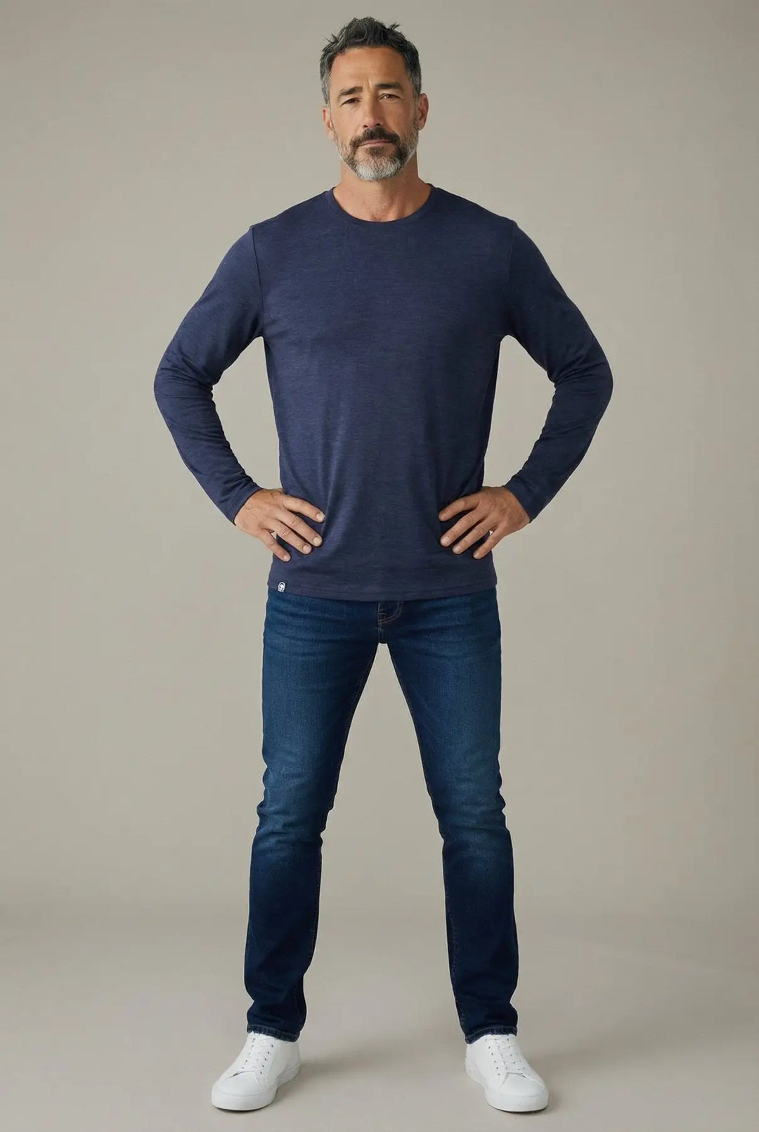 Man wearing a navy long-sleeve shirt and blue jeans on a beige background
