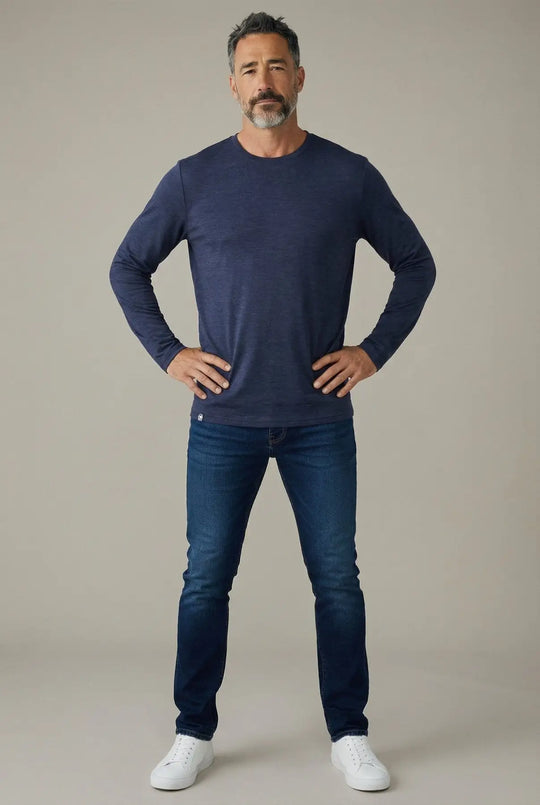 Man wearing a navy long-sleeve shirt and blue jeans on a beige background