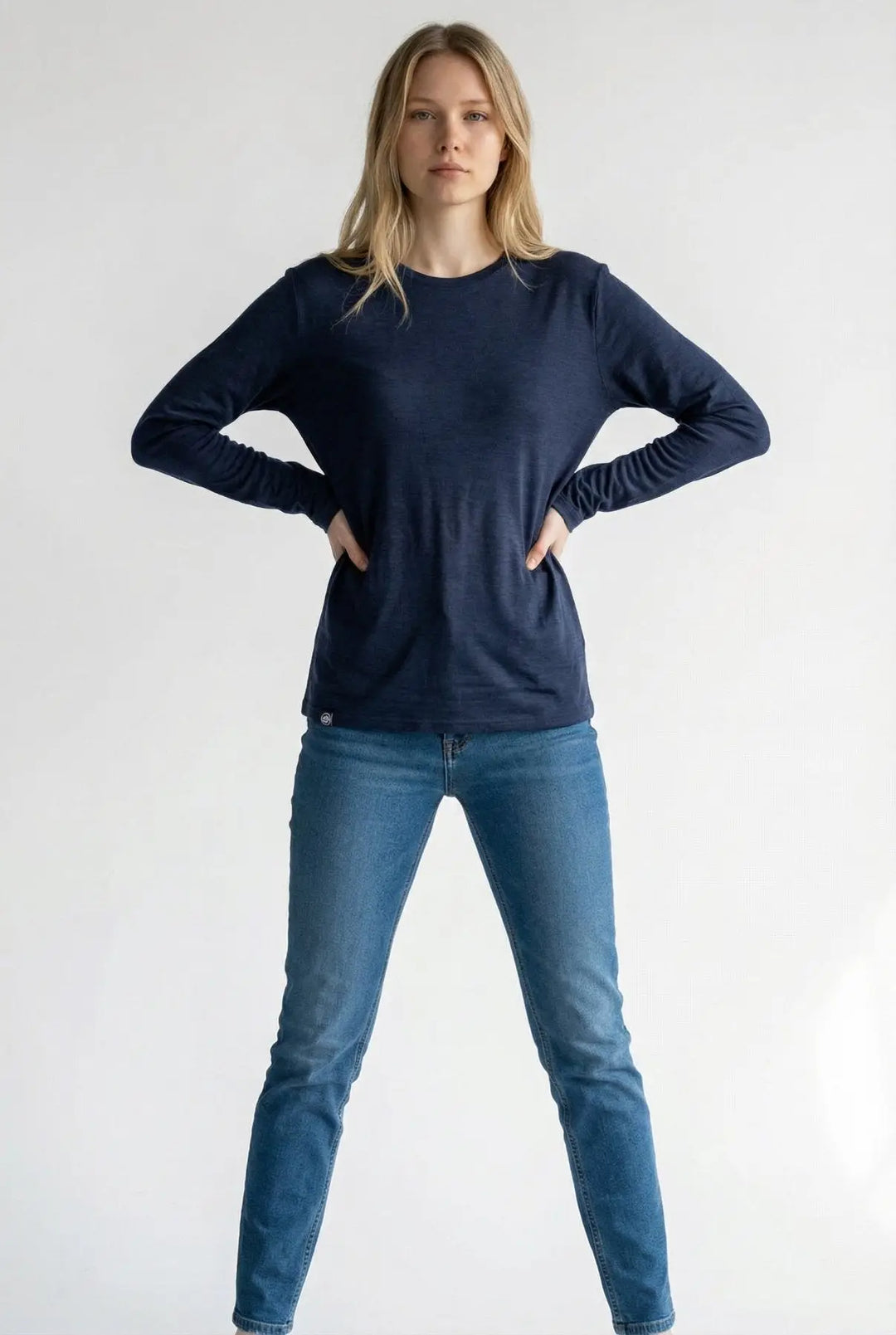 Woman wearing a navy long-sleeve shirt and blue jeans on a white background