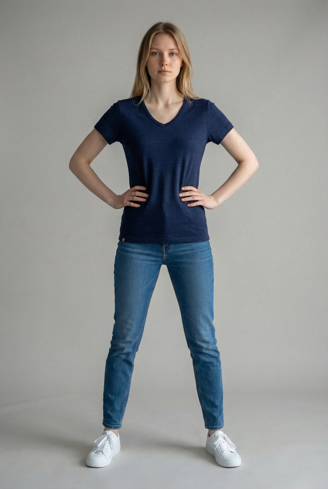 Woman wearing a navy blue t-shirt and blue jeans standing against a plain background