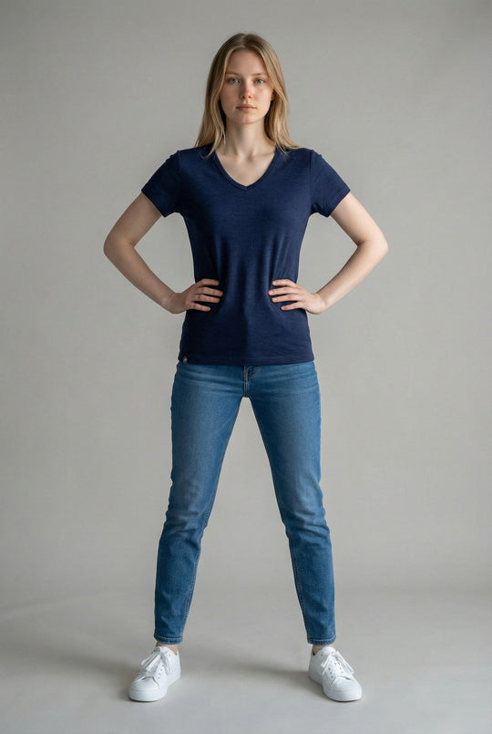 Woman wearing a navy blue t-shirt and blue jeans standing against a plain background