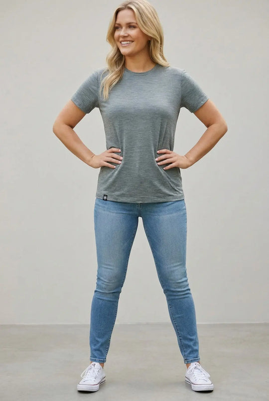 Woman wearing a gray t-shirt and blue jeans standing against a plain background