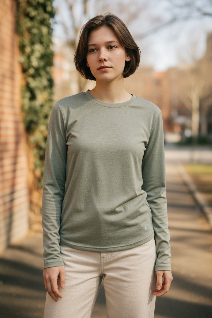 Woman wearing a green long-sleeve shirt standing outdoors with trees and a building in the background.