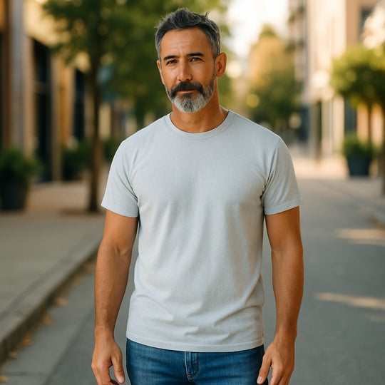 Man wearing a light blue t-shirt and blue jeans standing on a street.