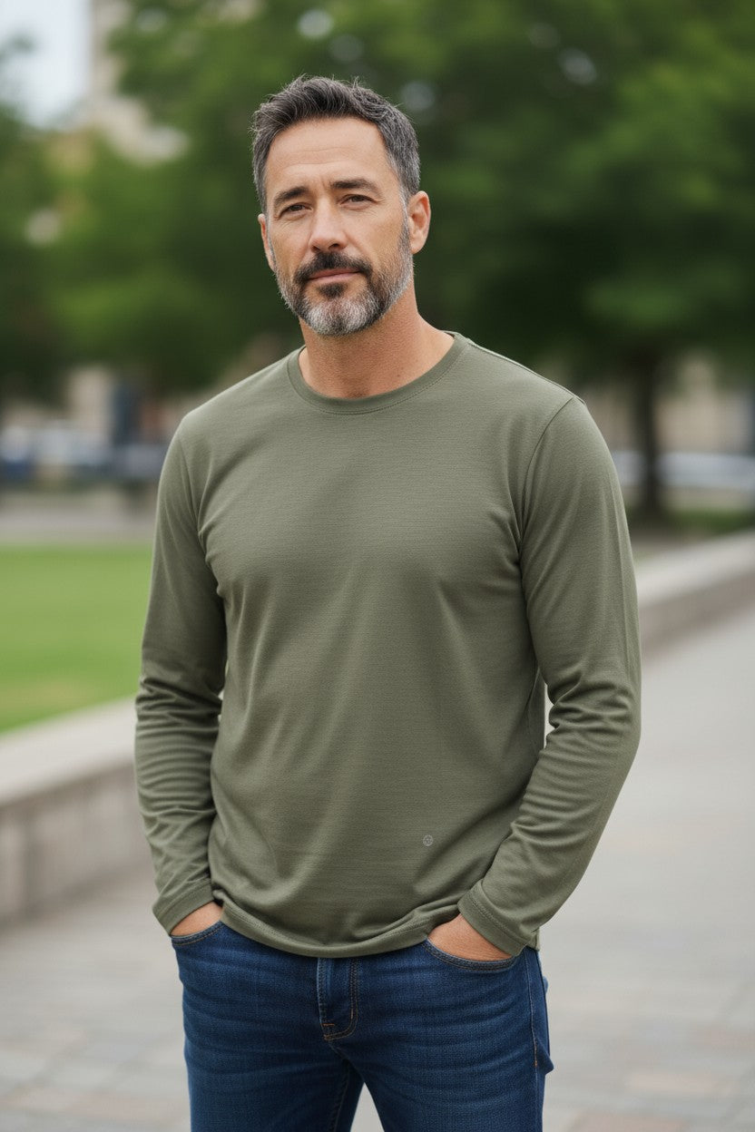 Man wearing a green long-sleeve shirt and blue jeans standing outdoors with trees in the background
