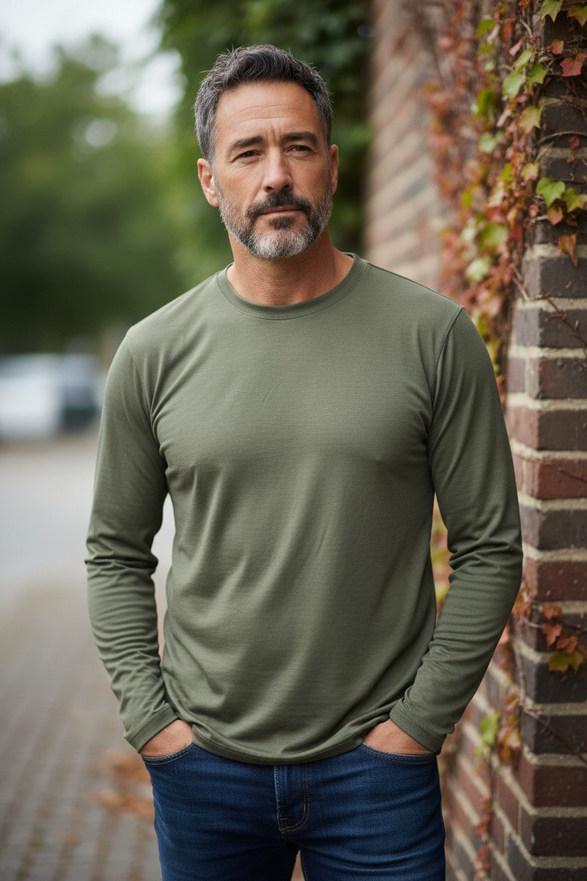 Man wearing a green long-sleeve shirt standing against a brick wall.